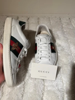 Vita Gucci ace bee - Snygga och ikoniska Gucci Ace Bee sneakers med klassiska gröna/röda web-stripes och broderad Gucci Bee 🐝. En tidlös modell med hög efterfrågan.  Detaljer:  ✔️ Märke: Gucci✔️ Modell: Ace Bee✔️ Storlek: EU 41 ✔️Färg: Vit / grön / röd✔️ Skick: Mycket bra begagnat skick✔️ Og: Gucci-kort medföljer  Normalt bruksslitage, främst lite smuts på sulan (se bilder). Inga sprickor eller trasiga sömmar – väl omhändertagna.      📦 Skickar snabbt. 💬hör av dig med frågor eller bud.