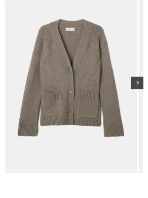 Beige kofta i ull från Wera - Mysig beige kofta från Wera i 100% ull. Koftan har v-ringning, stora ribbade fickor framtill och stängs med tre knappar. Långärmad modell med ribbade muddar vid ärmslut och nederkant. Perfekt för lager på lager under kyliga dagar.