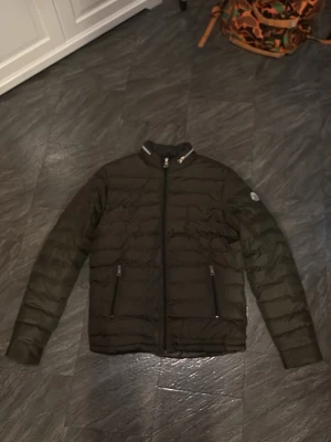 Svart Moncler pufferjacka herr S - Säljer en svart pufferjacka från Moncler i storlek S. Jackan har quiltad design, dragkedja framtill och två fickor med dragkedja. Klassisk Moncler-logga på ärmen och coolt innerfoder med serietidningsmotiv. Perfekt för dig som vill ha en lätt och snygg jacka. I detta fallet har jackan ett hål i armhålan som kan sys och bli väldigt bra skick 