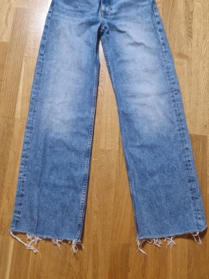 Blå broderade wide jeans från Monki - Säljer ett par ljusblå jeans från Monki med broderade blommor vid fickorna fram och bak. Byxorna har hög midja, raka vida ben och råa, fransiga benslut. Tillverkade i 100% bomull för en skön och avslappnad känsla. Storlek 26