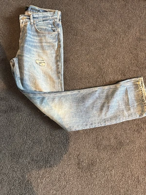 Straight jeans från 7 For All Mankind - Säljer ett par ljusblå straight fit jeans från 7 For All Mankind. Klassisk femficksmodell med slitningar och hål för en avslappnad vibe. Jeansen har normal midja och är gjorda i mjukt bomullsjeans-tyg. Perfekta till sneakers eller boots.