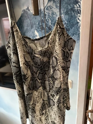 Ormskinnsmönstrad linnetopp från Amisu - Säljer en snygg linnetopp från Amisu i storlek S med coolt ormskinnsmönster i svart och beige. Toppen är ärmlös och har en rak, loose passform som ger en chill vibe. Perfekt för dig som gillar djurmönster och vill sticka ut lite extra.