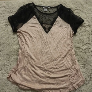 Beige blus med svart spets från H&M - Säljer en beige blus från H&M i storlek S med svart spets upptill och korta ärmar. Ovanpartiet har transparent mesh med prickigt mönster och v-ringad design. Perfekt för dig som gillar detaljer och kontraster i din outfit.