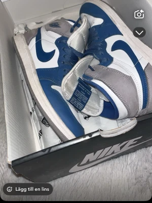 Nike Air Jordan 1 blå och grå - Säljer ett par Nike Air Jordan 1 i blått, vitt och grått. Skorna har klassisk hög siluett, snörning och ikoniska swoosh-loggan på sidan. Tillverkade i skinn och mocka för en clean och sportig look. Perfekta för dig som vill sticka ut med stil. Jag har tydligen betalat 2100kr men är glad och sälja den för 600kr, om de e något tveka inte o skriv 🫡
