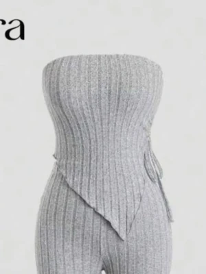 Grå ribbad bandeau tubtopp med knyt - Säljer en snygg grå bandeau tubtopp från shein med ribbad struktur och asymmetrisk nederkant. Toppen är ärmlös och har ett knyt i sidan för extra detalj. Perfekt att styla med höga jeans eller kjol för en trendig look.