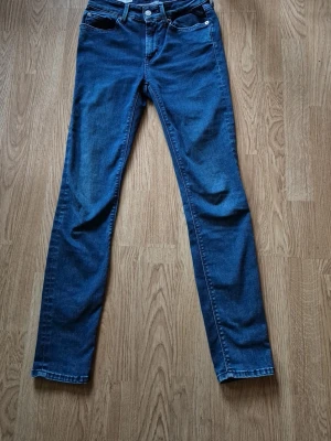 Replay blå jeans med broderad detalj - Snygga blå jeans från Replay med klassisk femficksdesign och broderad svart patch med blommor på bakfickan. Jeansen har en rak passform och är tillverkade i mjukt denim-material. Perfekt för dig som gillar stilrena och tidlösa jeans.