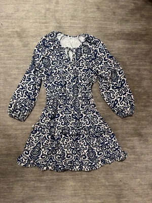 Somrig vit och blå mönstrad volang klänning - Säljer denna mönstrade vita och blåa sommarklänning som är köpt utomlands. Klänningen är endast använd ett fåtal gånger och är i ett mycket bra skick. Inga defekter eller tecken på användning. Köpt för ca 450 kr för två år sedan. Säljer nu för 230 kr men pris kan diskuteras. 💞💞