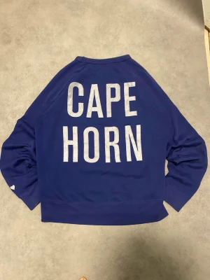 Acne studios sweatshirt - Blå sweatshirt från Acne studios med stor vit text på ryggen. Tröjan har långärmade och en liten vit hjärtdetalj på ena ärmen. Mjuk och skön bomullskvalitet, perfekt för chill dagar. Klassisk rund hals och loose passform.