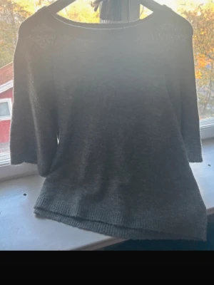 Grå stickad tröja från 157, M - Mysig grå stickad tröja från 157 i storlek M. Tröjan har en rund halsringning och trekvartsärmar, perfekt för lager-på-lager under kyliga dagar. Materialet är mjukt och har en ribbad kant nedtill och vid halsen. Enkel och stilren design som funkar till många outfits.