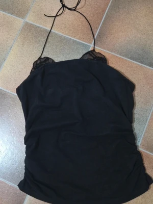 Linne Halterneck & Off Shoulder Crop Top Ribbat Stickat - Trendigt Linne i Kort Modell med Halterneck & Off Shoulder-detalj.  Säljer ett unikt och trendigt linne som kombinerar flera stilar i ett:  •Halterneck: För en snygg urringning i halsen.  •Off the Shoulder: Visar elegant axlarna.     •Crop Top: Kort och figurnära modell (Längd ca 43 cm  Tyget har en fin textur, vilket ger en fin stretch och passform. Denna stil är perfekt för vardags, sommarkvällar, festivaler, eller lager-på-lager styling.  Färg: Svart Storlek: M (Medium). 