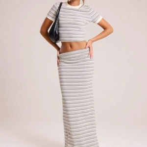 Randig långkjol i ljusa toner - Säljer en snygg långkjol med horisontella ränder i vitt, grått och beige. Kjolen har en rak och figurnära passform som ger en cool och avslappnad vibe. Perfekt att matcha med en croppad topp för en trendig look. Toppen säljes tillsammans!