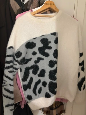 Vit och grå leopardmönstrad stickad tröja - Säljer en stickad tröja från Domus i vit och ljusgrå färg med coolt leopardmönster i svart. Tröjan har rund hals och långa ärmar, perfekt för dig som gillar att sticka ut med mönster. Mjuk och skön känsla, passar till jeans eller kjol.