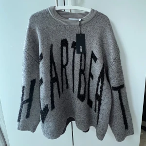 Snygg grå tröja - Säljer en grå oversized stickad tröja från Weekday med svart texten 'HEARTBEAT' över hela framsidan. 