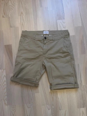 Beige shorts från Lindbergh White - Snygga beige shorts frän Lindbergh White i klassisk chino-stil. De har uppvikta benslut, bälteshällor, framfickor och bakfickor med knapp. Materialet är bomull med superflex för extra rörelsefrihet. Perfekta för varma dagar. Storlek M, riktigt sköna och nästan i nyskick. Använda 3 gänger, tvättade 1 gäng.