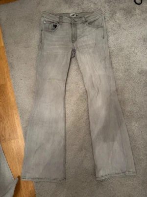 Grå bootcut jeans från 157, stl L - Snygga grå jeans från 157 i storlek L med bootcut-snitt och full längd. Klassisk femficksmodell med knapp och dragkedja fram. Jeansen är tillverkade i ett mjukt bomullsmaterial och har en neutral grå ton som passar till det mesta. Använd ett få tall gånger men fortfarande i riktigt bra skick, säljer då jag inte använder dem nått mer.