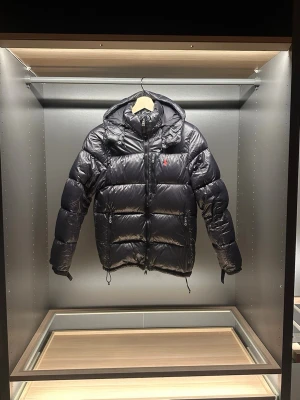 Polo Ralph Lauren puffer jacket - Svart pufferjacka från Polo Ralph Lauren med huva och tvåvägsdragkedja. Jackan har ett glansigt yttermaterial i polyester och är dekorerad med det klassiska röda Polo-logot på bröstet. Flera fickor med dragkedja och quiltad design för extra värme. Den har en liten defekt på ena armen men de är inget som syns så mycket. Hör av er vid frågor eller funderingar 