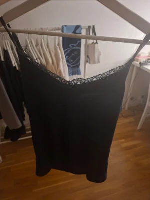 Svart linnetopp med spets från lager 157 - Säljer en svart linnetopp från 157 Black Label Collection i storlek M. Toppen har tunna axelband och en snygg spetskant upptill som ger en extra touch. Perfekt att styla med jeans eller kjol för en cool look.