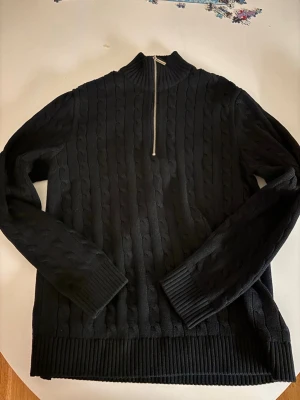 Svart stickad half zip tröja Selected - Svart stickad tröja från Selected med snygg kabelstickad struktur och half zip-dragkedja vid halsen. Tröjan har ribbade muddar och nederkant samt långärmad passform. Perfekt för dig som gillar stilrena och bekväma plagg.