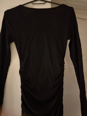 Svart långklänning från Gina Tricot - Svart långklänning från Gina Tricot i storlek XS. Klänningen har lång ärm, rundad halsringning och snygga rynkade detaljer längs sidorna. Materialet är mjukt och stretchigt, troligen bomull eller polyester. Perfekt för dig som gillar stilrena och enkla plagg.