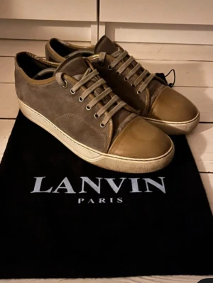 Beige sneakers från Lanvin Paris - Snygga sneakers från Lanvin Paris i beige mocka med matchande snörning och gummitå i en ljusare ton. Skorna har en rund tå och vit platt sula som ger en clean look. Perfekta för dig som gillar stilrena och exklusiva sneakers. Kontakta vid minsta intresse!!!! Priset kan diskuteras vid snabb affär🔥🔥🔥