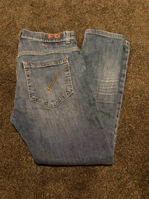 Dondup George jeans - Snygga blå jeans från Dondup modell george med klassisk femficksdesign och slitna detaljer på ena benet. Jeansen har en Slim passform och normal midja, med ljusare tvättade partier och kontrastsömmar. Perfekta för dig som gillar Dondups! Längd: 91cm passar mig som är 174cm 60kg