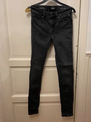 Replay svarta skinny jeans - Svarta Replay jeans med skinny fit och klassisk femficksdesign. Jeansen har en mörk tvätt och smal passform som sitter tajt längs benen. Materialet är stretchigt jeans och de har dragkedja och knapp i midjan. Perfekta för dig som gillar en stilren och modern look.