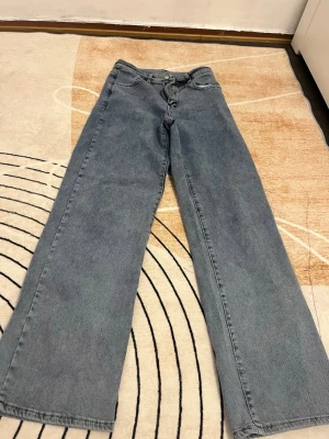 Blå wide jeans med rak passform - Säljer ett par blå jeans med breda ben och rak passform. Klassisk femficksmodell med knapp och dragkedja framtill. Jeansen har en enkel design utan synliga detaljer och är tillverkade i jeansmaterial.