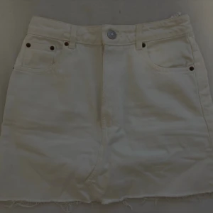 Vit kortkjol från Zara - Säljer en vit kortkjol från Zara i storlek S. Kjolen har klassisk jeansstil med fem fickor, knapp och dragkedja framtill samt rå kant nedtill för en cool look. Perfekt att matcha med sneakers eller boots för en avslappnad vibe.
