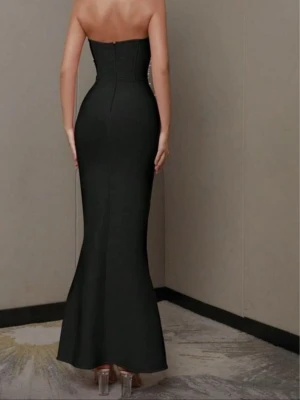 Svart långklänning med pärldetaljer - Supersnygg svart långklänning med figurnära passform och axelbandslös design. Överdelen är dekorerad med vita pärlor som ger en lyxig känsla. Klänningen har en lätt utsvängd nederdel och dragkedja i ryggen. Perfekt för dig som vill sticka ut med elegans.