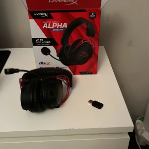 HyperX Cloud Alpha Wireless - Det kostar 800 igentligen.HyperX Cloud Alpha Wireless gaming headset med upp till 300 timmars batteritid, trådlös USB-mottagare och avtagbar mikrofon. Headsetet och tillbehör ser ut att vara i mycket gott skick, inga synliga defekter eller slitage. Perfekt för spel och kommunikation.