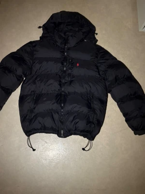 Svart pufferjacka från Polo Ralph Lauren - Säljer en helt ny svart Polo-jacka i storlek S. Jackan är aldrig använd – tyvärr för stor för mig. Perfekt skick! Pris: 700 kr (kan diskuteras, gärna bud mellan 650–700 kr) Hör av dig vid intresse! 