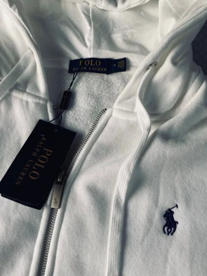 Vit Ralph lauren zip hoodie  - Säljer min vita Ralph lauren zip hoodie som är helt ny. Taggen är kvar och den är använd en gång. Anledningen till varför jag säljer den är då den inte passar mig. Storlek M. 