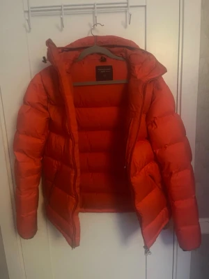 Orange pufferjacka Peak Performance S - Säljer en orange pufferjacka från Peak Performance i storlek S. Jackan har huva, tre dragkedjefickor och en schysst puffad look. Perfekt för kalla dagar och har en riktigt snygg färg som sticker ut. Materialet är syntet och dun.