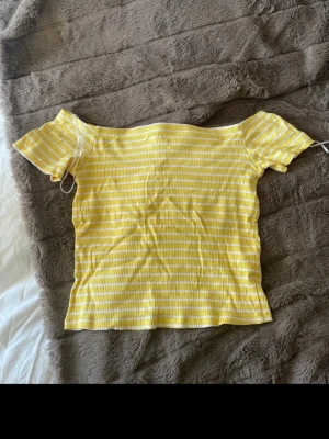 Gul och vit randig offshoulder topp - Säljer en söt gul och vit randig topp från H&M Divided i storlek M. Modellen är offshoulder med korta ärmar och ribbad struktur. Perfekt för varma dagar och har en fräsch, ungdomlig vibe.