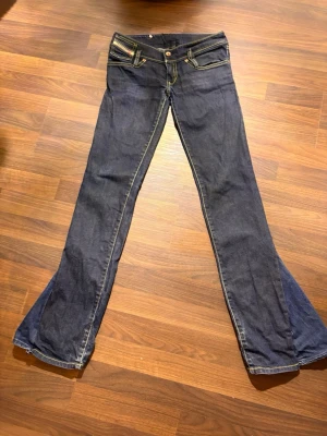 Bootcut jeans från Diesel, mörkblå - Snygga mörkblå bootcut jeans från Diesel med kontrasterande gula sömmar och klassiska fem fickor. Jeansen har låg midja och är tillverkade i jeansmaterial. Perfekt för dig som gillar en retro vibe och vill sticka ut med en cool siluett.