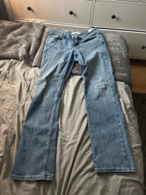 Blå wide jeans från Junkyard, stl S - Säljer ett par ljusblå jeans från Junkyard i storlek S. Modellen är wide med raka ben och klassisk femficksdesign. Materialet är 78% bomull, 21% återvunnen bomull och 1% elastan för lite stretch. Perfekt för dig som gillar avslappnad stil.