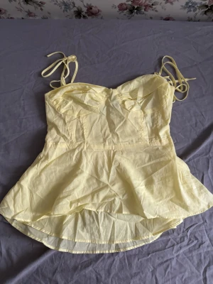 Ljusgul linnetopp med knytband - Säljer en ljusgul linnetopp med tunna axelband som knyts upptill. Toppen har en söt och feminin form med lätt utsvängd nederdel och markerad byst. Materialet är tunt och luftigt, perfekt för varma dagar. Passar dig som gillar en fräsch och somrig look. Priset kan diskuteras och fråga för fler bilder 