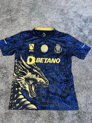 Blå FC Porto tröja - Säljer en blå FC Porto matchtröja i storlek S från AFRM med ett fett drakmotiv i guldig och blått. Tröjan har guldiga detaljer, tryck med BETANO och Super Bock samt klubbmärken på bröstet. Perfekt för dig som vill sticka ut på läktaren eller hemma.