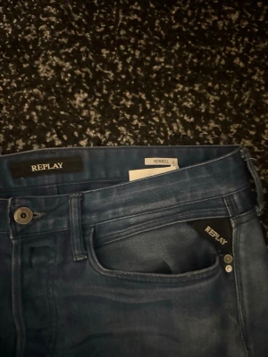 Replay Newbill blå jeans - Snygga blå jeans från Replay, modellen Newbill. Jeansen har klassisk femficksdesign, raka ben och en cool tvätt med ljusare partier. Passar dig som gillar stilrena och bekväma jeans med lite attityd. Materialet är jeans och de har metallknapp och nitar vid fickorna. Knappt använt.