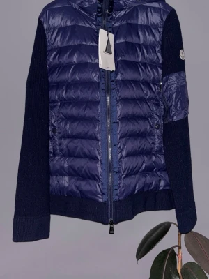 Helt ny Mörkblå cardigan från Moncler - Helt ny snygg mörkblå cardigan från Moncler med stickade ärmar och quiltad front. Jackan har dragkedja framtill och en klassisk Moncler-logga på ärmen. Perfekt för dig som vill ha en stilren och sportig look med exklusiv känsla.