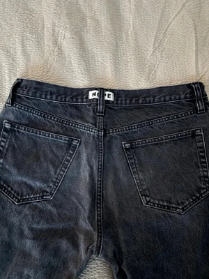 Svarta raka jeans från HOPE - Säljer ett par svarta jeans från HOPE med klassisk femficksdesign och raka ben. Jeansen har en mörk tvätt och tydliga sömmar, samt bälteshällor med HOPE-logga bak. Materialet är robust denim i bomull och passformen är normal med straight cut.