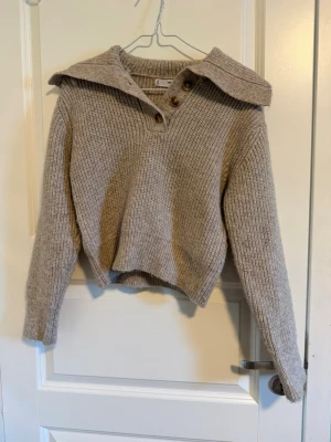 Beige stickad tröja med krage - Säljer en beige stickad tröja från Mango med bred krage och tre knappar framtill.