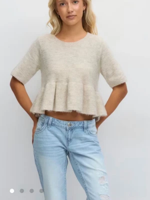 Beige stickad croppad topp med volang - Superfin beige stickad topp med korta ärmar och volang nedtill. Modellen är croppad och har en rund halsringning. Perfekt för dig som gillar en söt och trendig stil. Skriv om ni vill ha flera bilder 