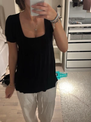 Svart blus med fyrkantig ringning - Säljer en svart blus med korta puffärmar och snygg fyrkantig ringning. Blusen har en lätt rynkad struktur och är i en luftig modell som ger en avslappnad men ändå stilren look. Perfekt att matcha med både jeans och kjol.