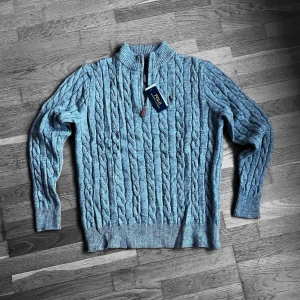 Grå stickad tröja Polo Ralph Lauren - Säljer en grå kabelstickad tröja från Polo Ralph Lauren med half zip och ribbad krage. Tröjan har långärmad passform och är tillverkad i mjukt ullmaterial. Klassisk logga broderad på bröstet och snygga detaljer vid dragkedjan. Perfekt för kyliga dagar.