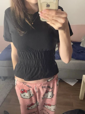 Svart topp från Collusion - Säljer en svart topp från Collusion med smockad midja som ger en snygg form. Toppen har korta ärmar och är tillverkad i mjukt bomullsmaterial. Enkel och stilren design som funkar till många olika looks.