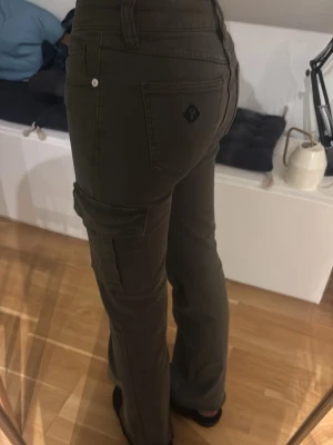 Mörkgröna bootcut A-brand cargopants - Säljer ett par mörkgröna cargopants från A-brand med bootcut. Byxorna har normal passform. Har tyvärr en limpistol fläck på vänstra låret, går säkert att få bort dem man försöker!