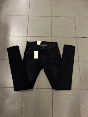 Svarta slimmade jeans W30 L32 - Svarta jeans med tight passform och smal fot. Klassisk femficksmodell med läderpatch bak i midjan. Jeansen har en stilren look och är gjorda i ett stretchigt denim-material som sitter snyggt och bekvämt hela dagen.