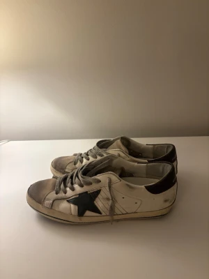 Golden Goose vita sneakers med stjärna - Halloj. Jag säljer nu mina riktigt feta goolden goose som jag haft i runt ett halvår. Dom är köpta ifrån merch Sweden för 4500kr. Dom är i rätt så gott skick men de finns några slitningar och som ni ser på 3 bilden så är sulan trasig men provisionallt limmad. Hör gjärna av er☺️