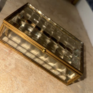 Smyckeskrin - Bilderna visar en glasask med guldfärgade metallkanter och rutmönstrad design, inte en väst.